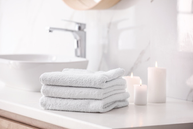 Photo of Stack of fresh towels and burning candles on countertop in bathroom