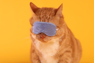 Photo of Cute ginger cat with sleep mask on orange background