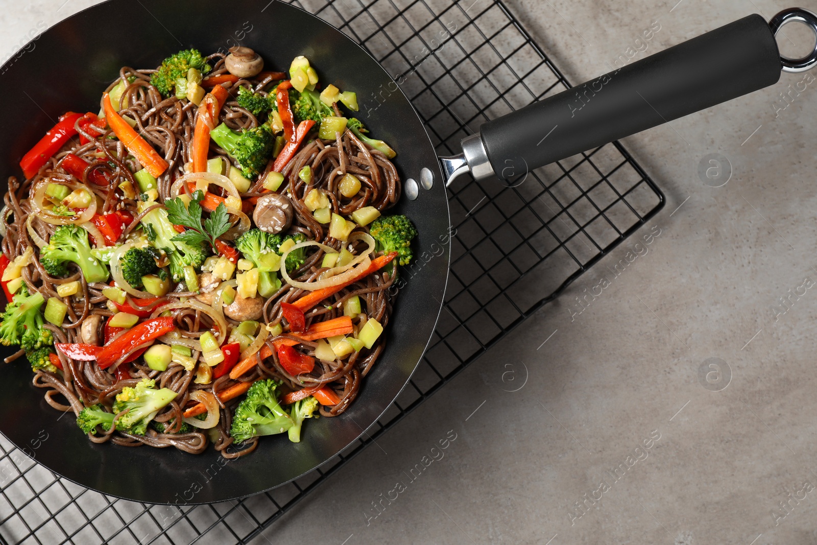 Photo of Stir-fry. Tasty noodles with meat and vegetables in wok on grey textured table, top view