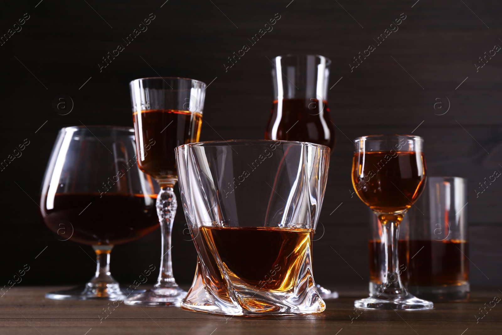 Photo of Different delicious liqueurs in glasses on wooden table