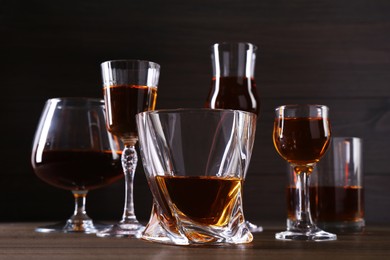 Different delicious liqueurs in glasses on wooden table