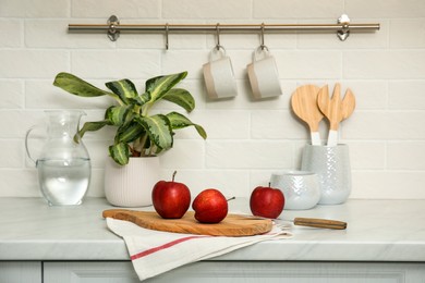 Clean towel and wooden board with ripe apples on countertop in kitchen