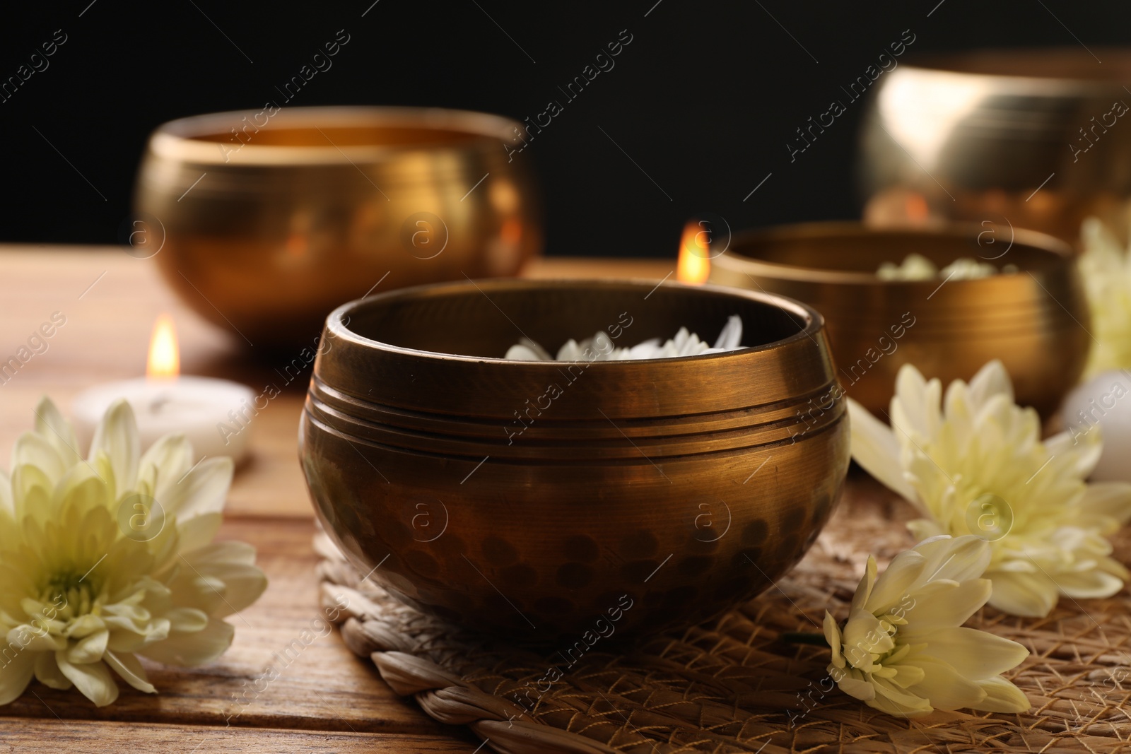 Photo of Tibetan singing bowls and beautiful chrysanthemum flowers on wooden table, closeup
