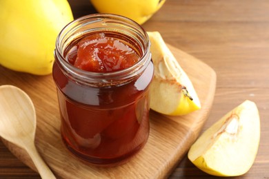 Photo of Tasty homemade quince jam in jar and fruits on wooden table, closeup