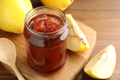 Tasty homemade quince jam in jar and fruits on wooden table, closeup