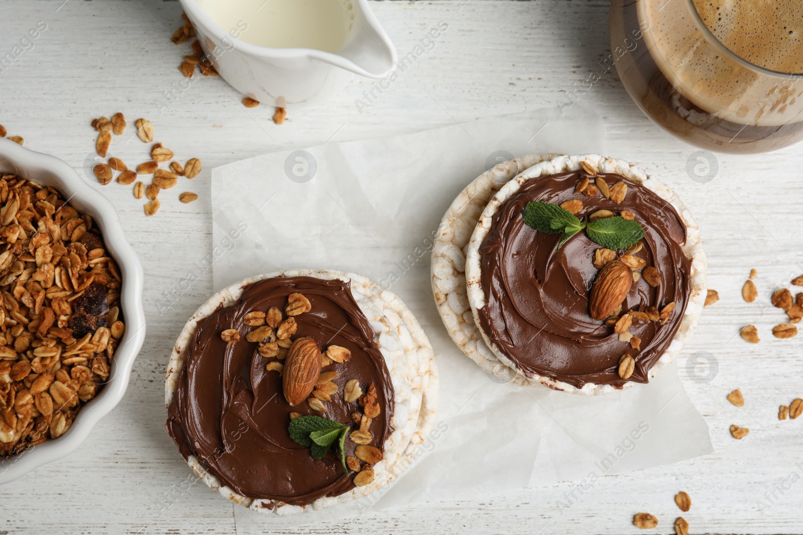 Photo of Puffed rice cakes with chocolate spread on white wooden table, flat lay