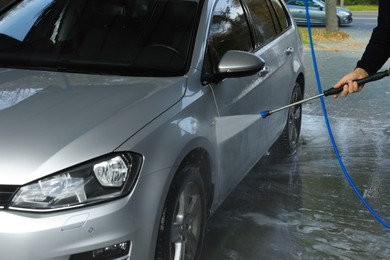 Photo of Man washing auto with high pressure water jet at outdoor car wash, closeup