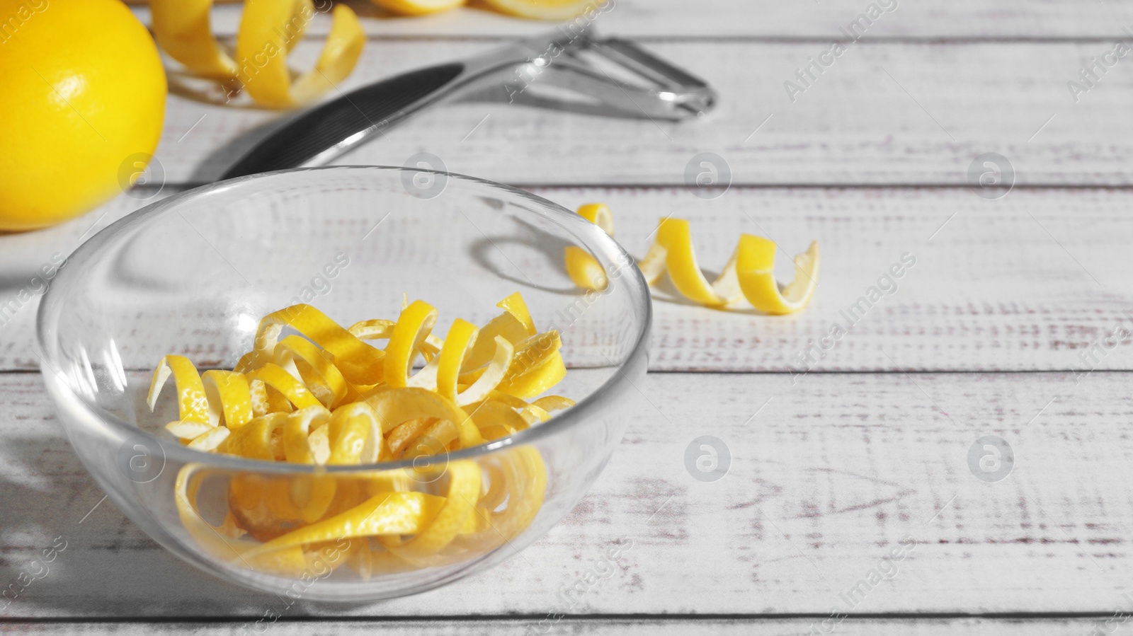 Photo of Bowl with peel pieces, fresh lemons and zester on white wooden table. Space for text