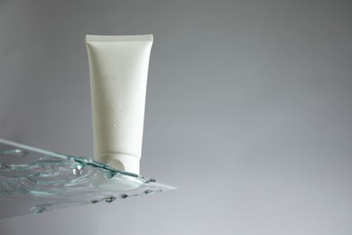 Photo of Tube with moisturizing cream on glass against grey background, low angle view. Space for text