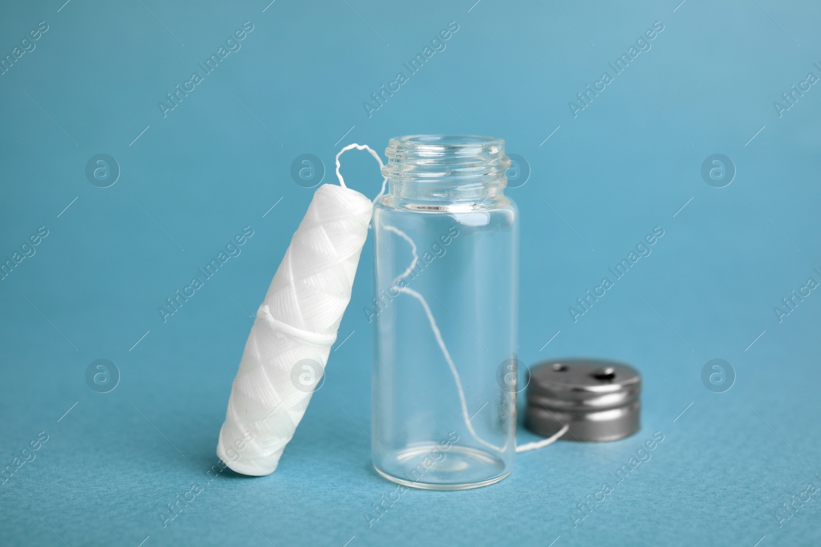 Photo of Biodegradable dental floss and glass jar on light blue background