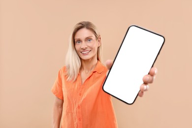 Photo of Happy woman holding smartphone with blank screen on beige background