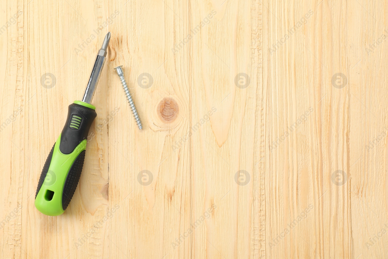 Photo of Screwdriver with green handle and screw on wooden table, flat lay. Space for text