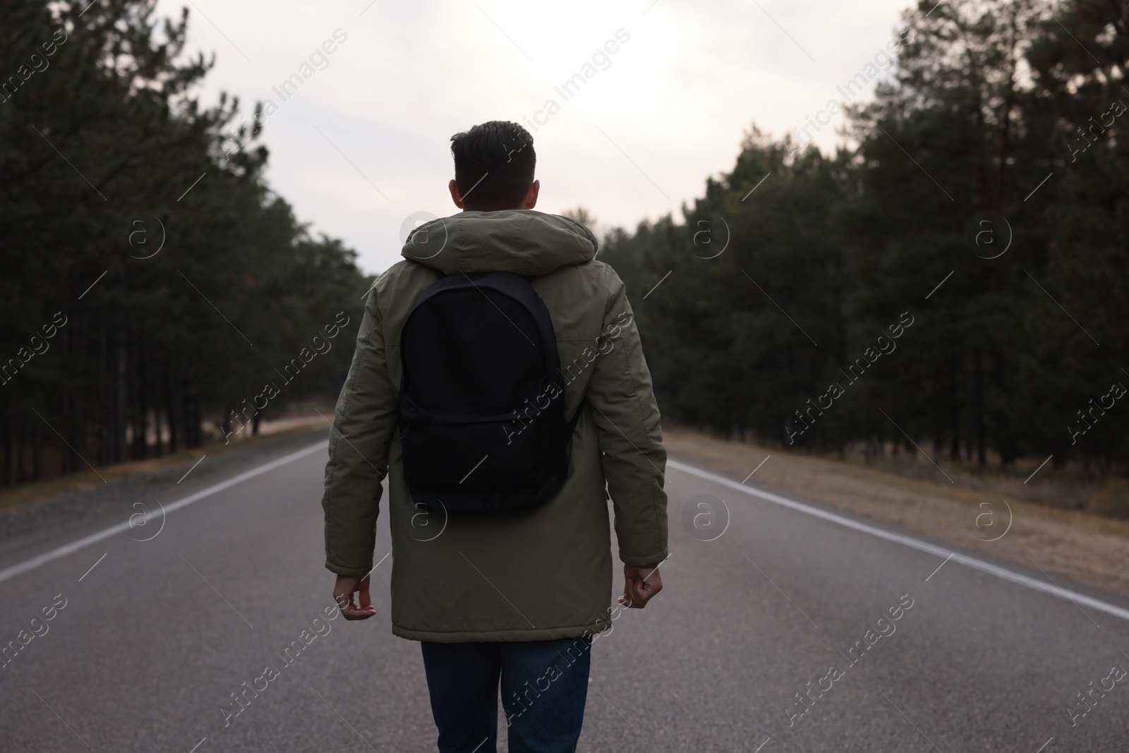 Photo of Man with backpack on road near forest, back view