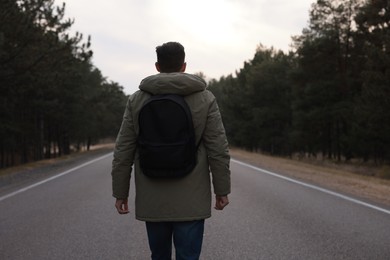 Man with backpack on road near forest, back view