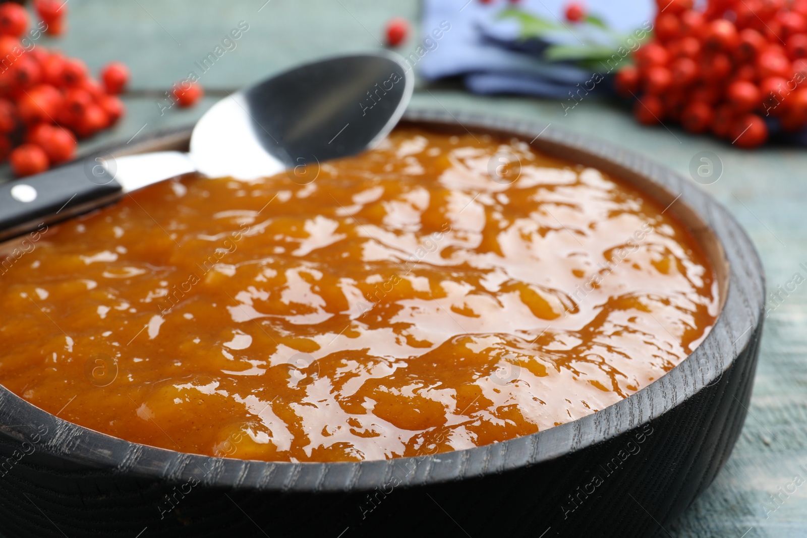 Photo of Delicious rowan jam in wooden bowl on light blue table, closeup