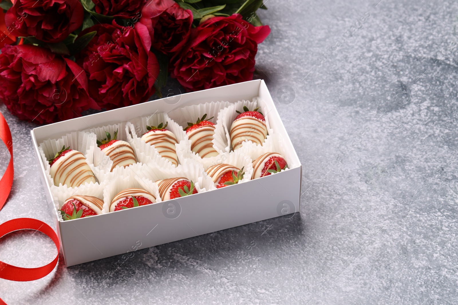 Photo of Delicious chocolate covered strawberries in box and flowers on light grey table. Space for text