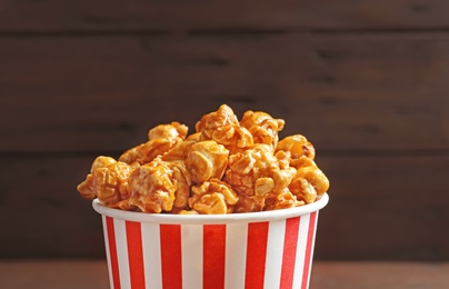Photo of Delicious popcorn with caramel in paper bucket on dark background, closeup