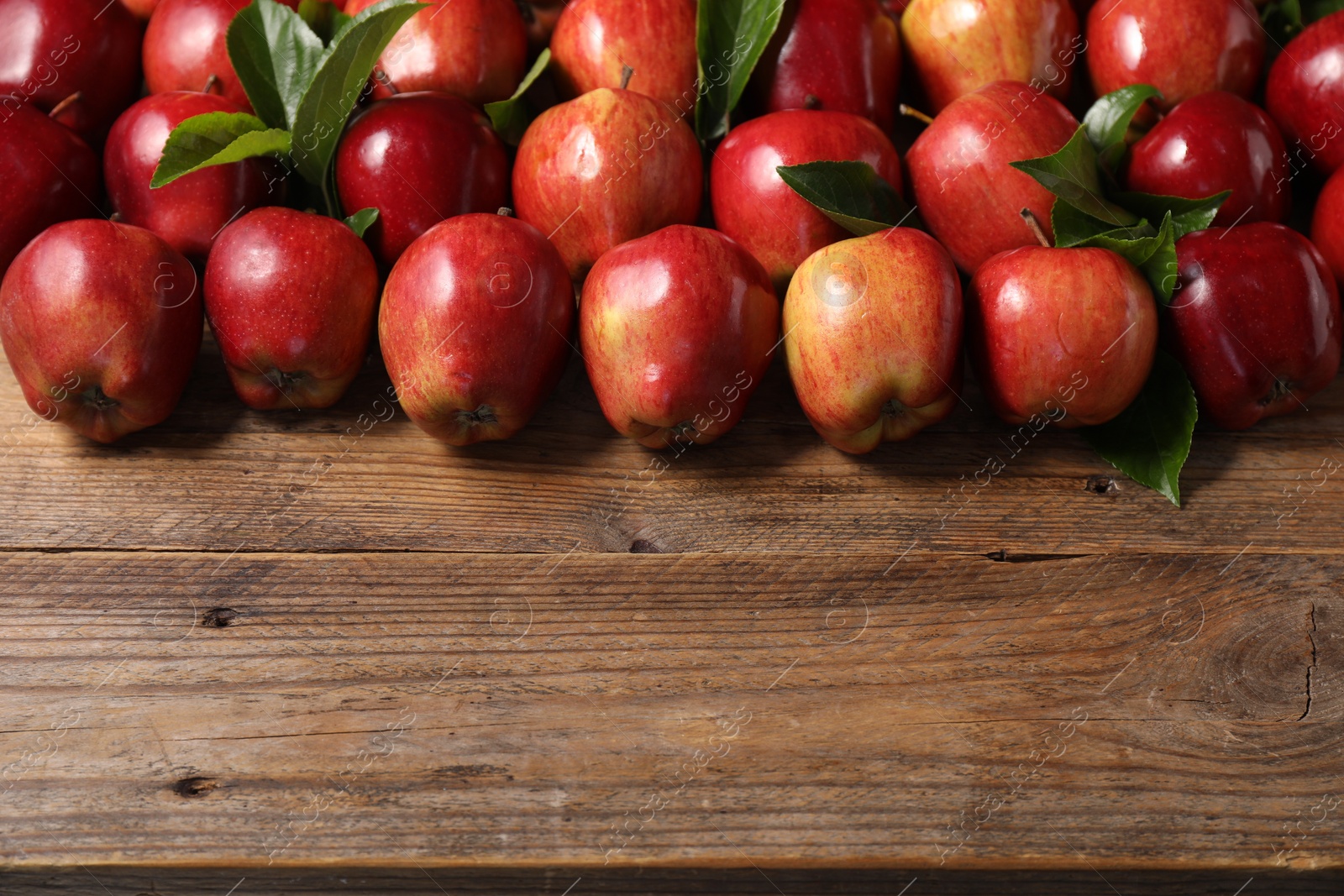 Photo of Fresh ripe red apples and leaves on wooden table. Space for text