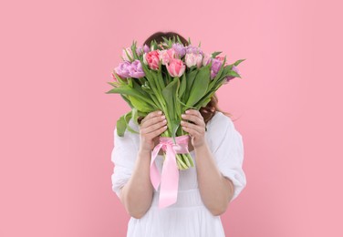 Young woman holding bouquet of beautiful tulips on pink background