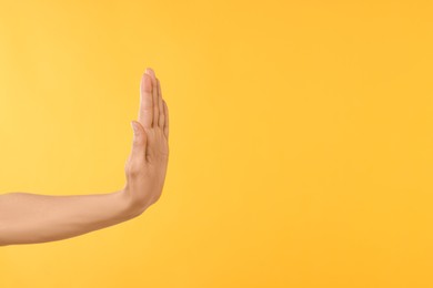 Woman showing stop gesture on yellow background, closeup. Space for text
