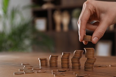 Photo of Woman stacking coins at wooden table indoors, closeup