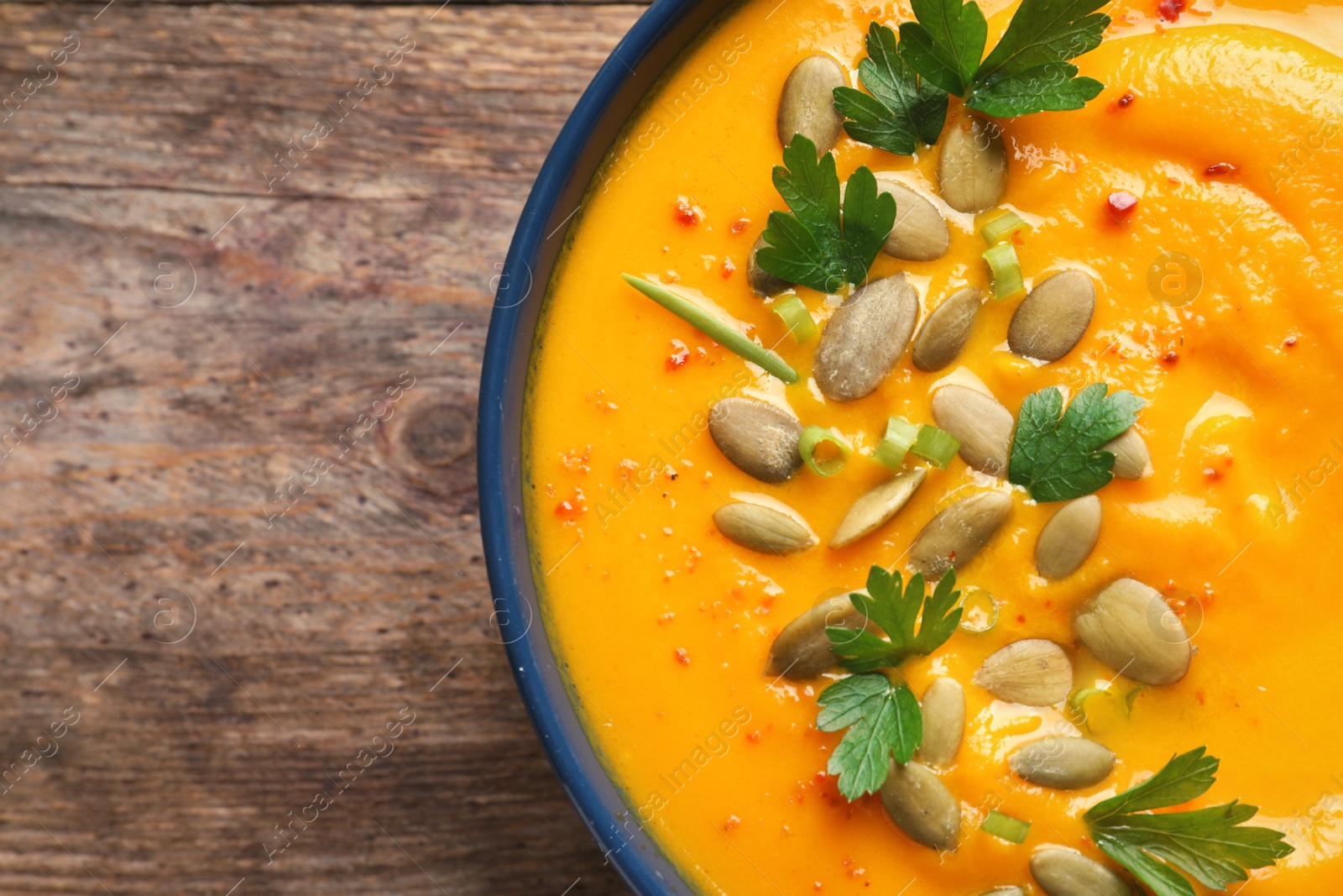 Photo of Delicious pumpkin cream soup in bowl on wooden background, top view. Space for text