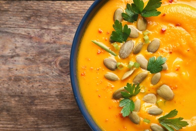 Delicious pumpkin cream soup in bowl on wooden background, top view. Space for text