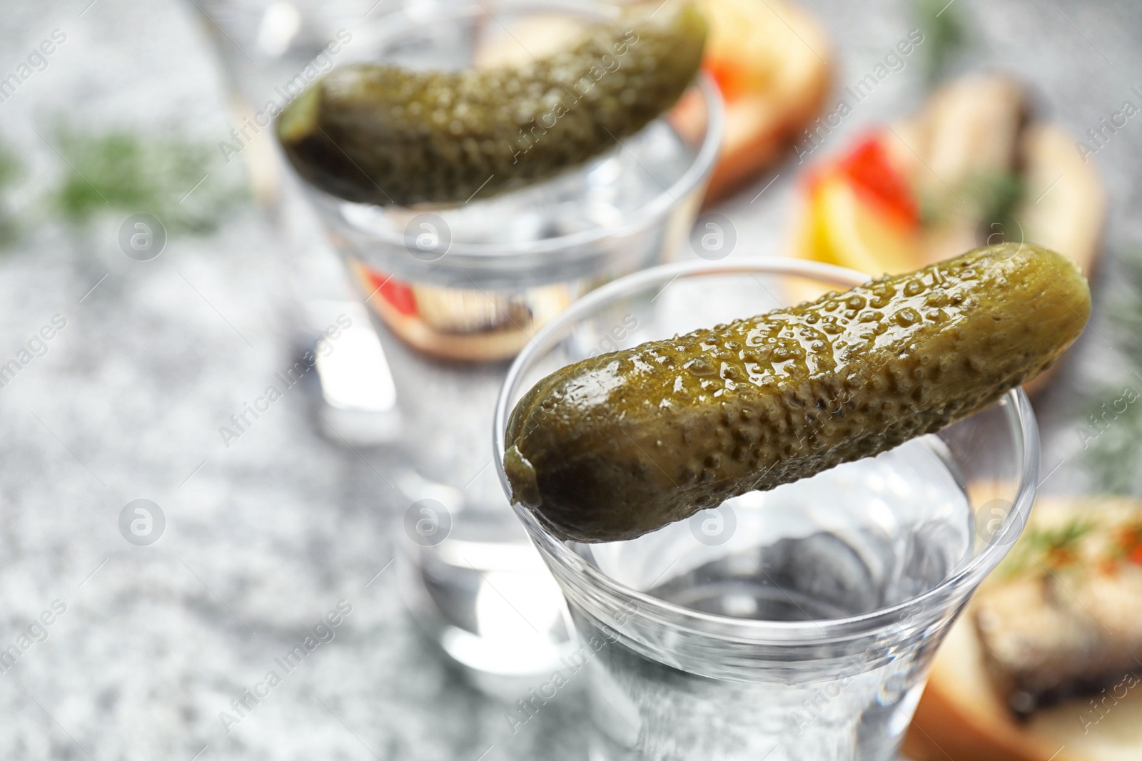 Photo of Cold Russian vodka with pickles on grey table, closeup