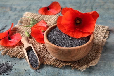 Wooden bowl of poppy seeds, scoop and flowers on color table