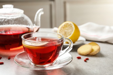 Photo of Glass cup of healthy goji tea with lemon on grey table. Space for text