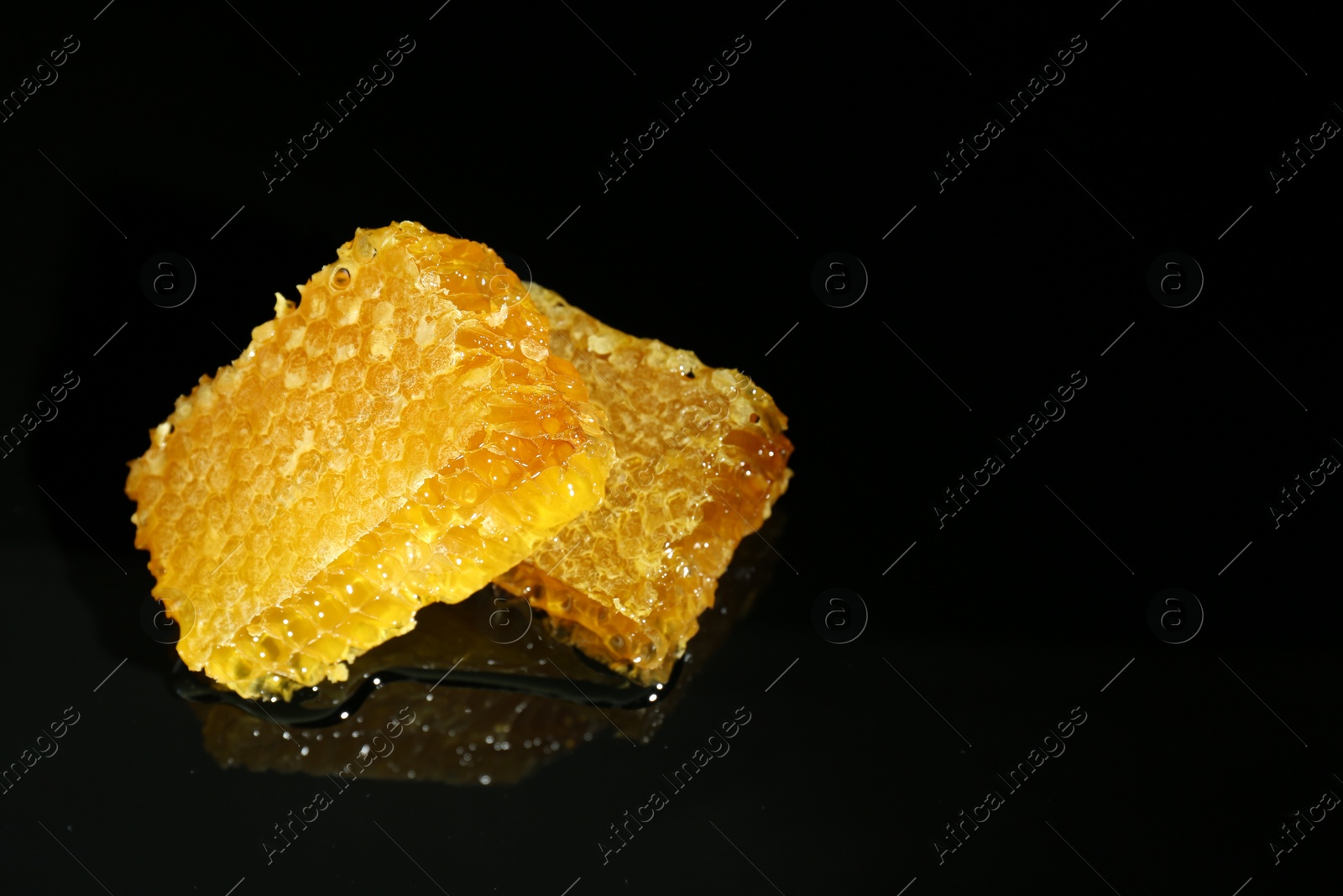 Photo of Natural honeycombs with tasty honey on black background, space for text