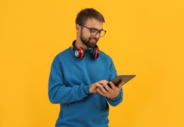 Photo of Student with headphones using tablet on yellow background