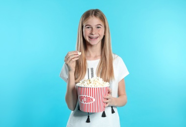 Teenage girl with popcorn during cinema show on color background