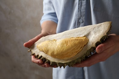 Woman holding piece of ripe durian fruit on grey background, closeup