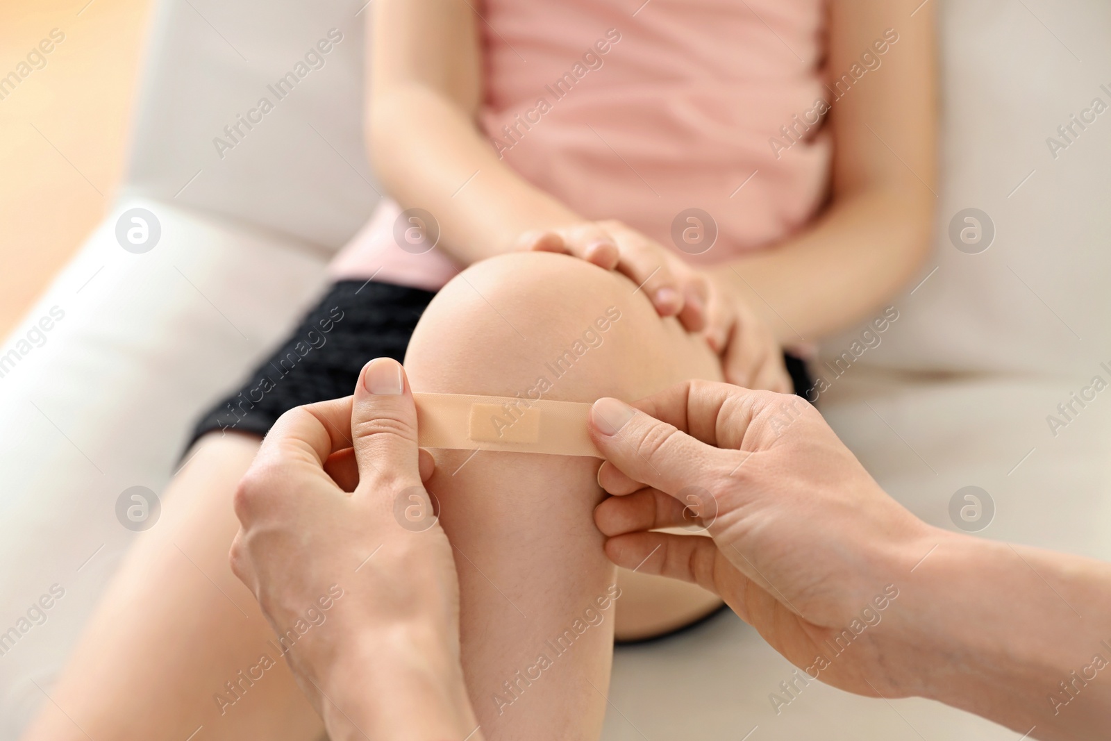 Photo of Doctor applying medical patch on little patient's injured knee indoors, closeup