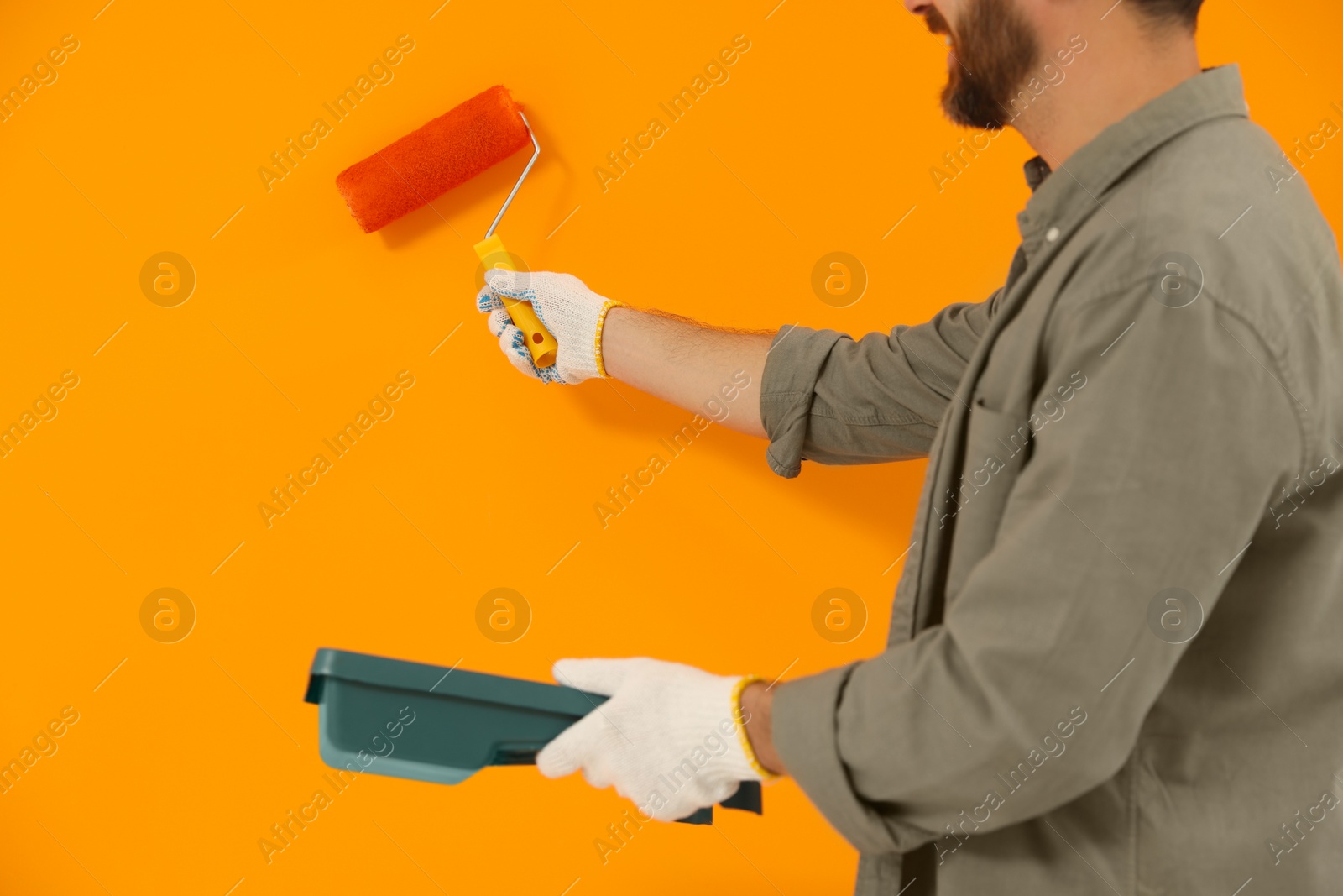 Photo of Designer painting orange wall with roller, closeup