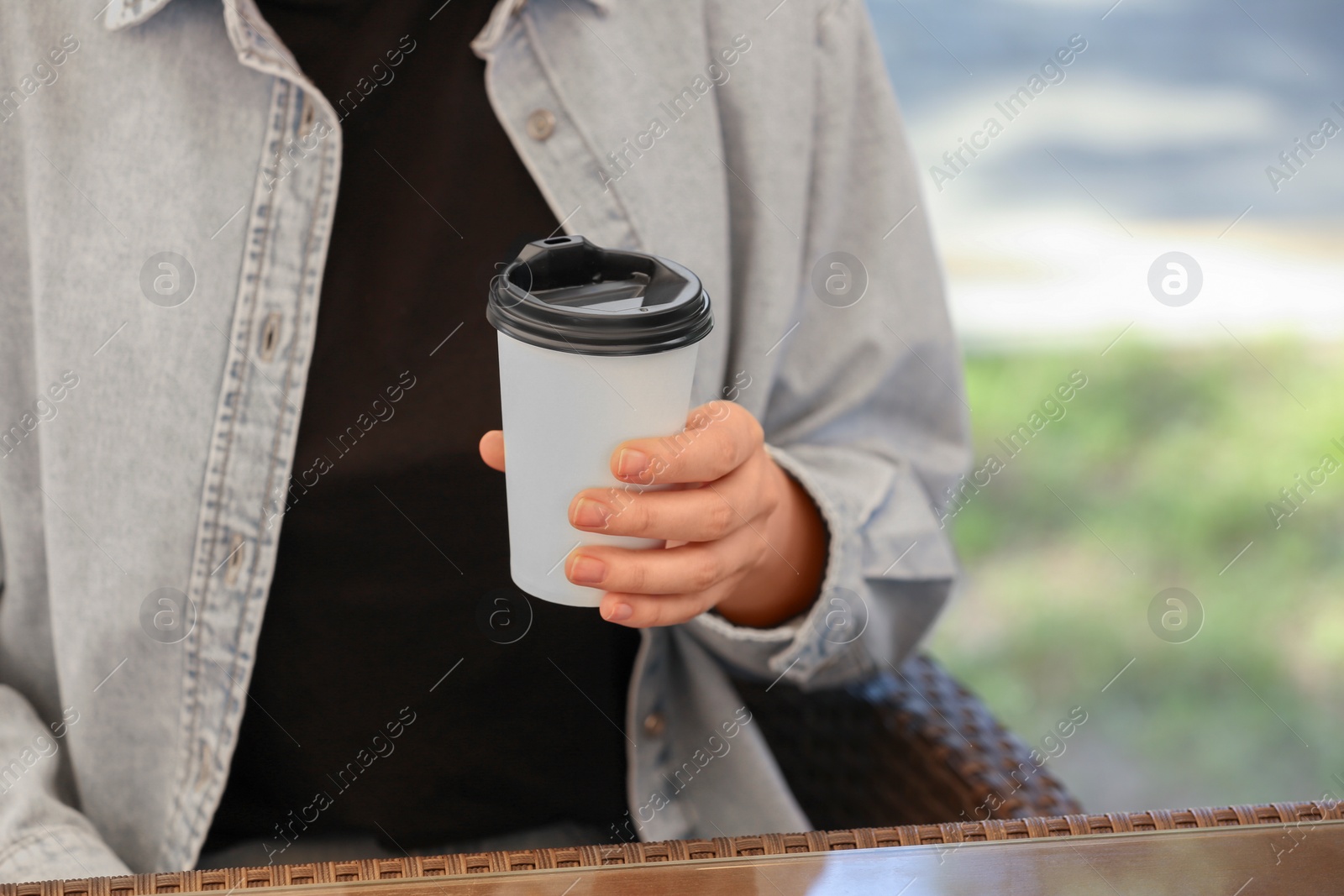 Photo of Woman holding takeaway paper cup at table, closeup and space for text. Coffee to go