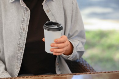 Photo of Woman holding takeaway paper cup at table, closeup and space for text. Coffee to go
