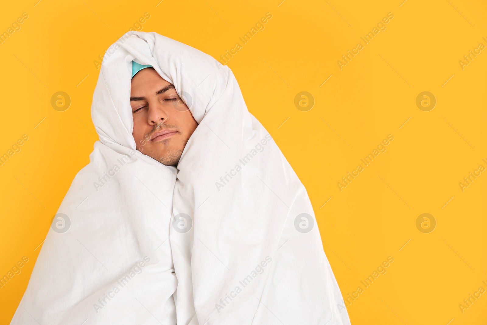 Photo of Man wrapped in blanket sleeping on yellow background. Space for text