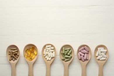 Photo of Different vitamin capsules in spoons on white wooden table, flat lay. Space for text