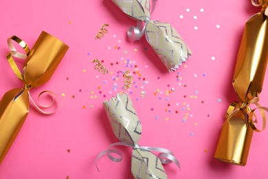 Photo of Open and closed Christmas crackers with shiny confetti on pink background, flat lay