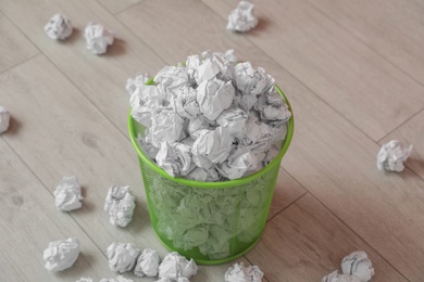 Photo of Full trash bin and crumpled paper on wooden floor