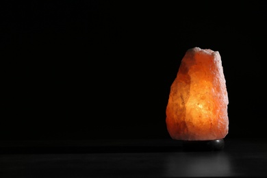 Himalayan salt lamp on table against black background. Space for text