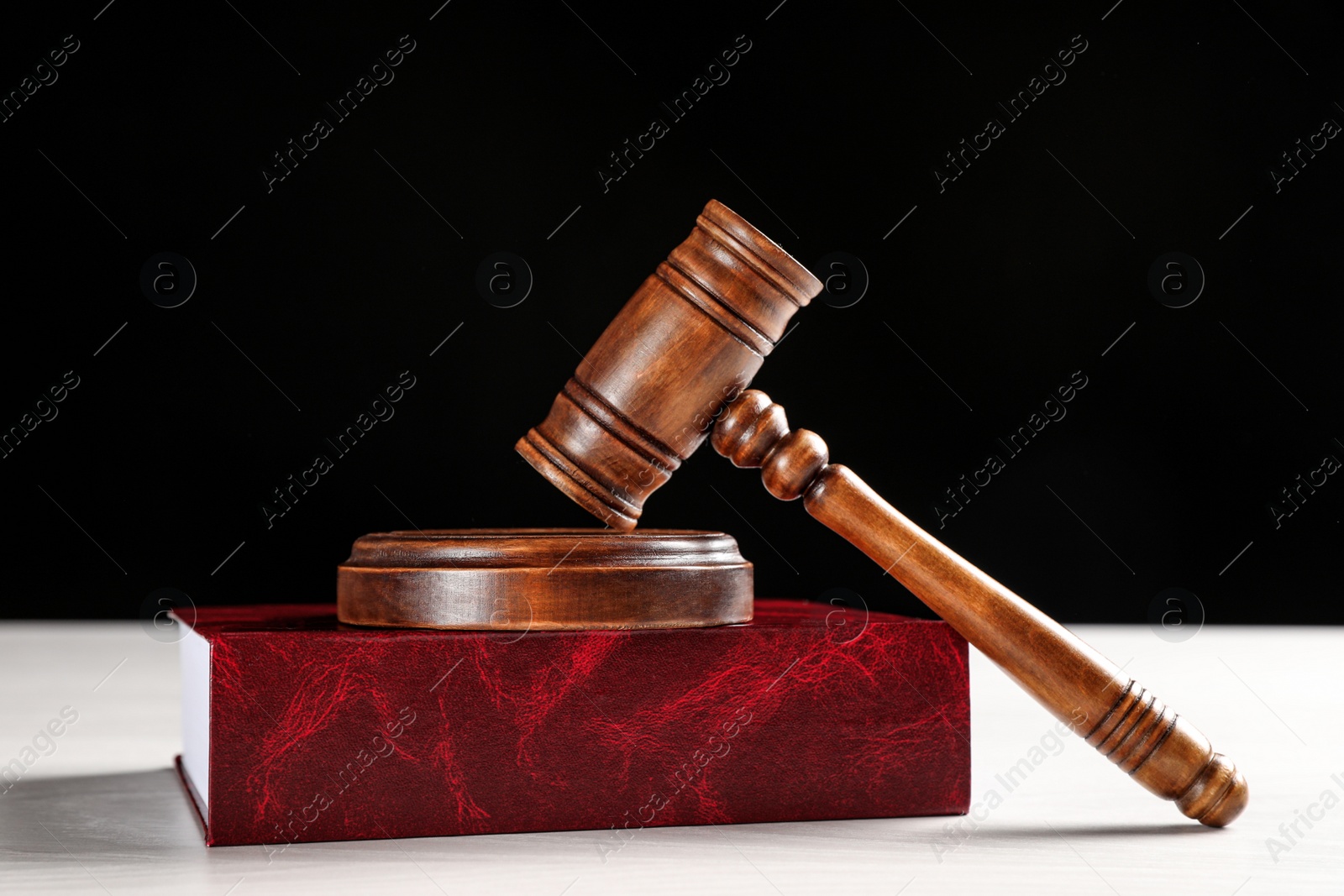 Photo of Judge's gavel and book on white table against black background. Criminal law concept