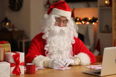 Santa Claus signing Christmas letters at table in room