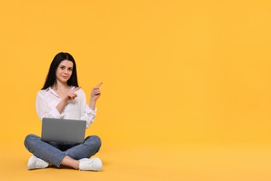 Photo of Student with laptop sitting and pointing at something on yellow background. Space for text