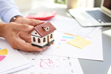 Photo of Man holding house model at table, closeup. Property tax