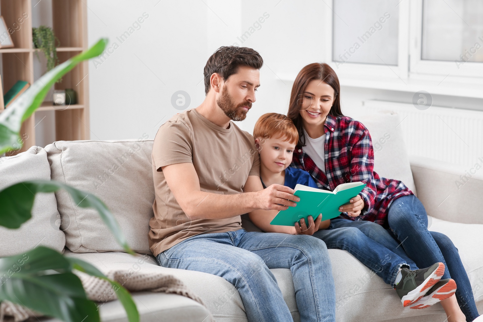 Photo of Happy parents with their child reading book on couch at home