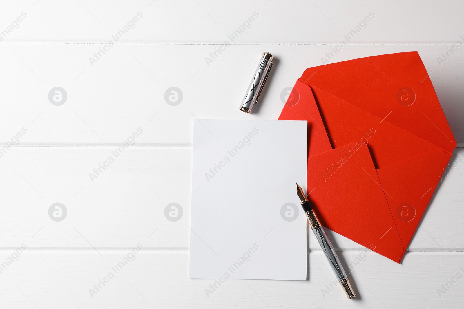 Photo of Blank sheet of paper, pen and letter envelope on white wooden table, top view. Space for text