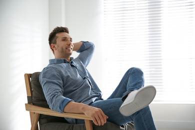 Young man relaxing in armchair near window at home